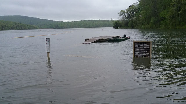 (image) Boat Launch Area parking lot,  loop with pavement crumped and area litered with debris and restroom in the background.