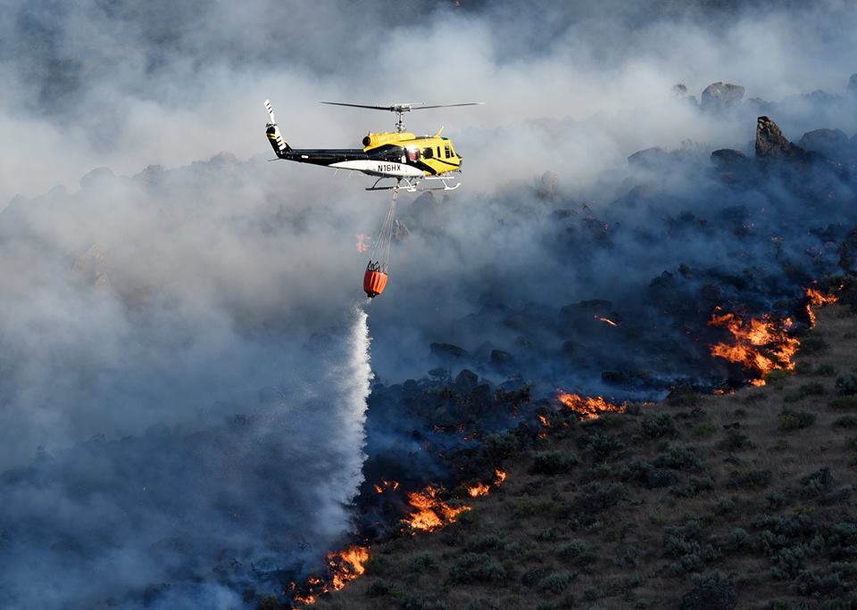helicopter dropping water on a flaming front