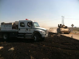 photo of Engine 441 in the black of a wildfire with a tank and humvee driving past.