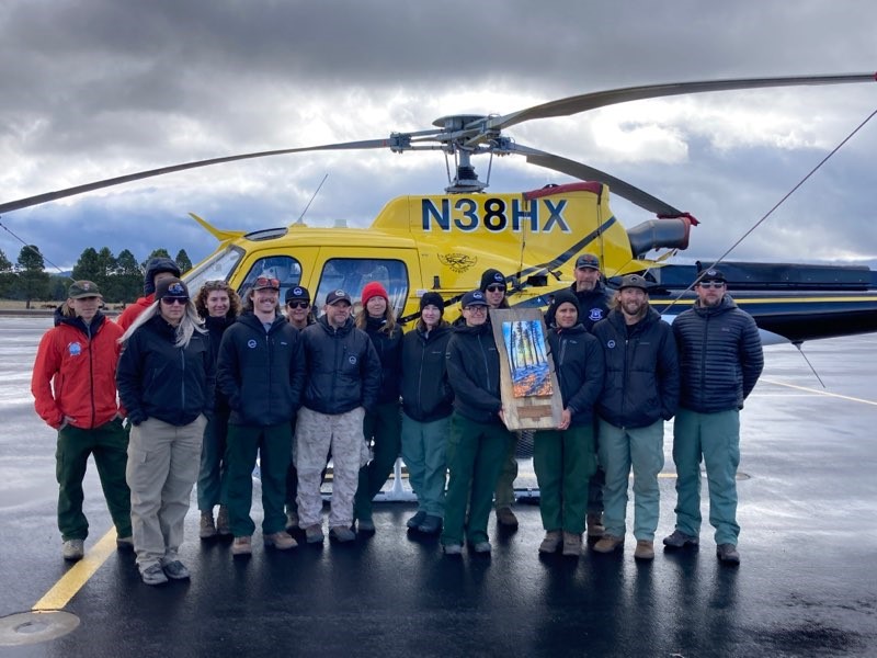Crewmembers pose in from of helicopter with recognition plaque