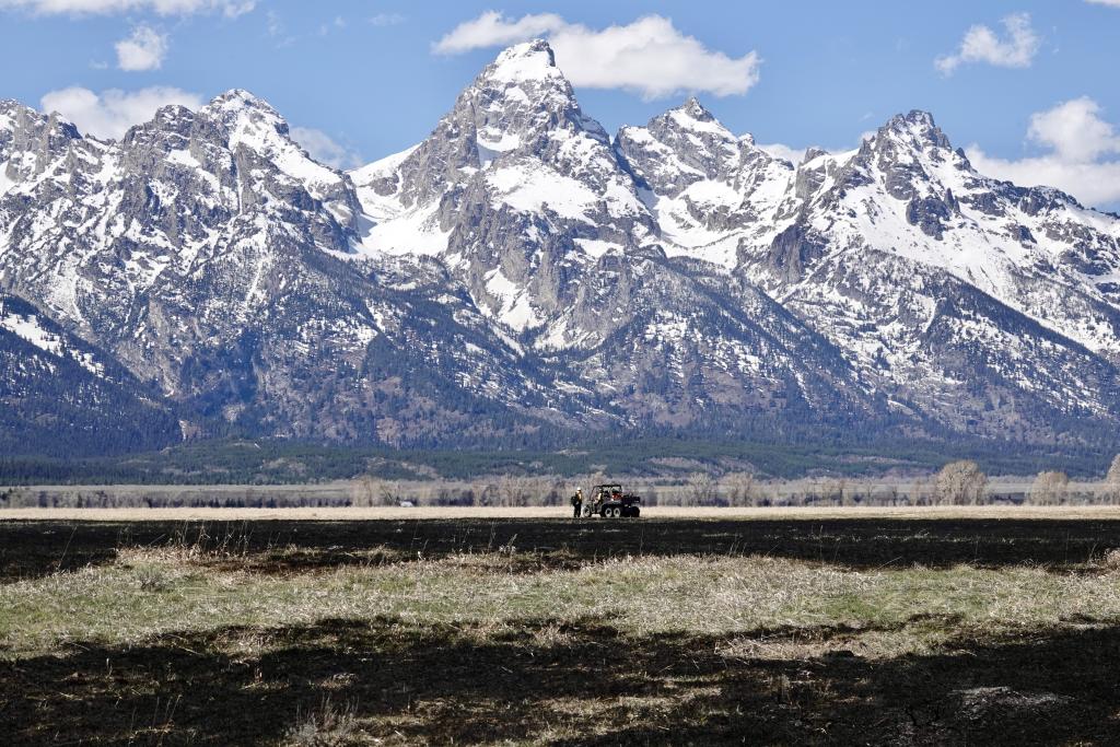 Snow covered Teton mountain range with patches of blackened grass and UTV in foreground